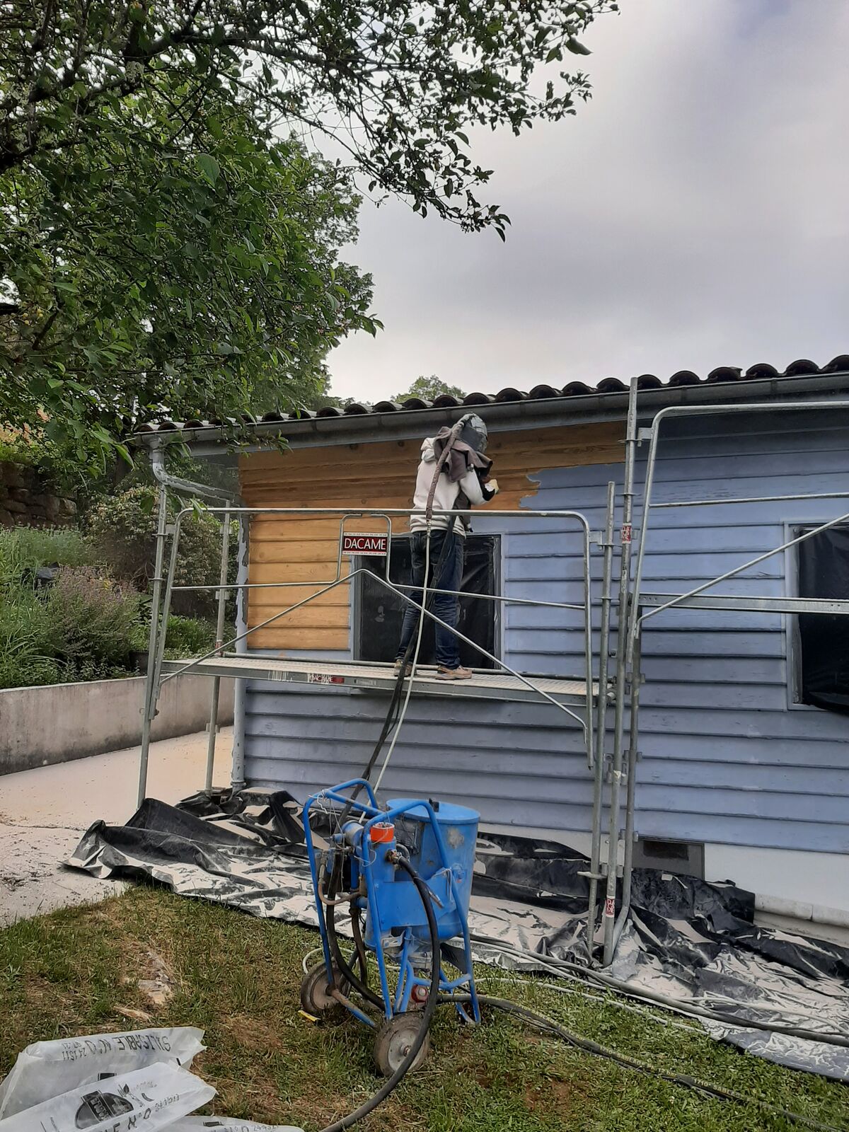 Sablage d'un bardage de façade en bois depuis un échafaudage, machine de sablage au premier plan