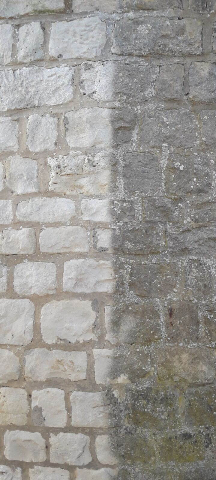 Mur en pierre de taille nettoyé sur une moitié, la limite entre pierre propre et pierre encrassée est nette